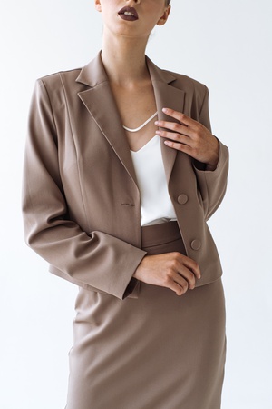 КОСТЮМ ЮБКА ДО КОЛЕН И ПРИТАЛЛЕНЫЙ ЖАКЕТ НА ФОНЕ КАПУЧИНО